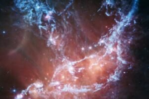 This new infrared image of NGC 346 from NASA’s James Webb Space Telescope’s Mid-Infrared Instrument (MIRI) traces emission from cool gas and dust. In this image blue represents silicates and sooty chemical molecules known as polycyclic aromatic hydrocarbons, or PAHs. More diffuse red emission shines from warm dust heated by the brightest and most massive stars in the heart of the region. Bright patches and filaments mark areas with abundant numbers of protostars. This image includes 7.7-micron light shown in blue, 10 microns in cyan, 11.3 microns in green, 15 microns in yellow, and 21 microns in red (770W, 1000W, 1130W, 1500W, and 2100W filters, respectively).