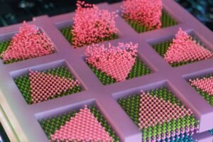 MIT engineers have developed a method to seamlessly stack electronic layers to create faster, denser, more powerful computer chips. The team deposits semiconducting particles (in pink) as triangles within confined squares, to create high-quality electronic elements, directly atop other semiconducting layers (shown in layers of purple, blue, and green). Credits:Credit: Cube 3D Graphic